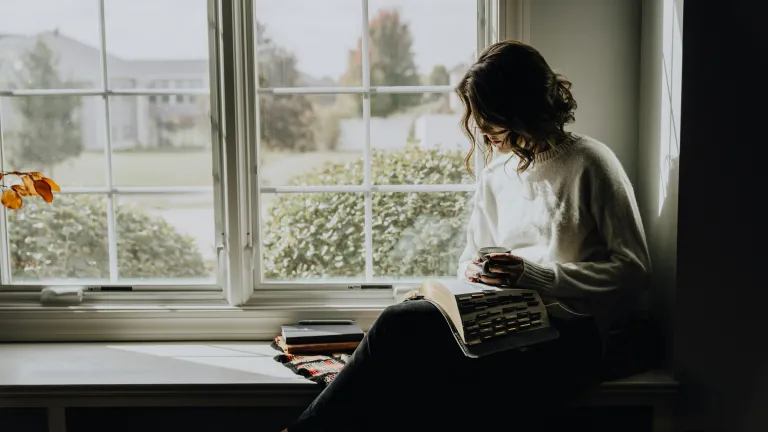 A woman reading her Bible by a window.