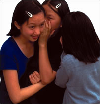 Three teenage girls whispering to each other.